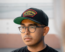 Load image into Gallery viewer, man wearing - suavecito hat with yellow embroidered text and red border outline &quot;suavecito m.f.g. california&quot;
