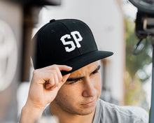 Load image into Gallery viewer, man wearing - black suavecito hat with white embroidered text &quot;SP&quot;
