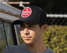 Load image into Gallery viewer, man wearing - black suavecito hat with white embroidered text and red background &quot;suavecito pomade inc.&quot;

